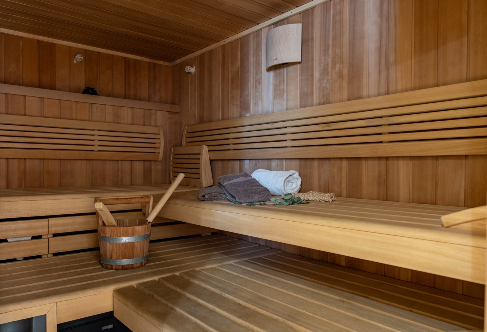 Intérieur d’un sauna en bois, avec seau, louche et serviettes pliées sur les bancs