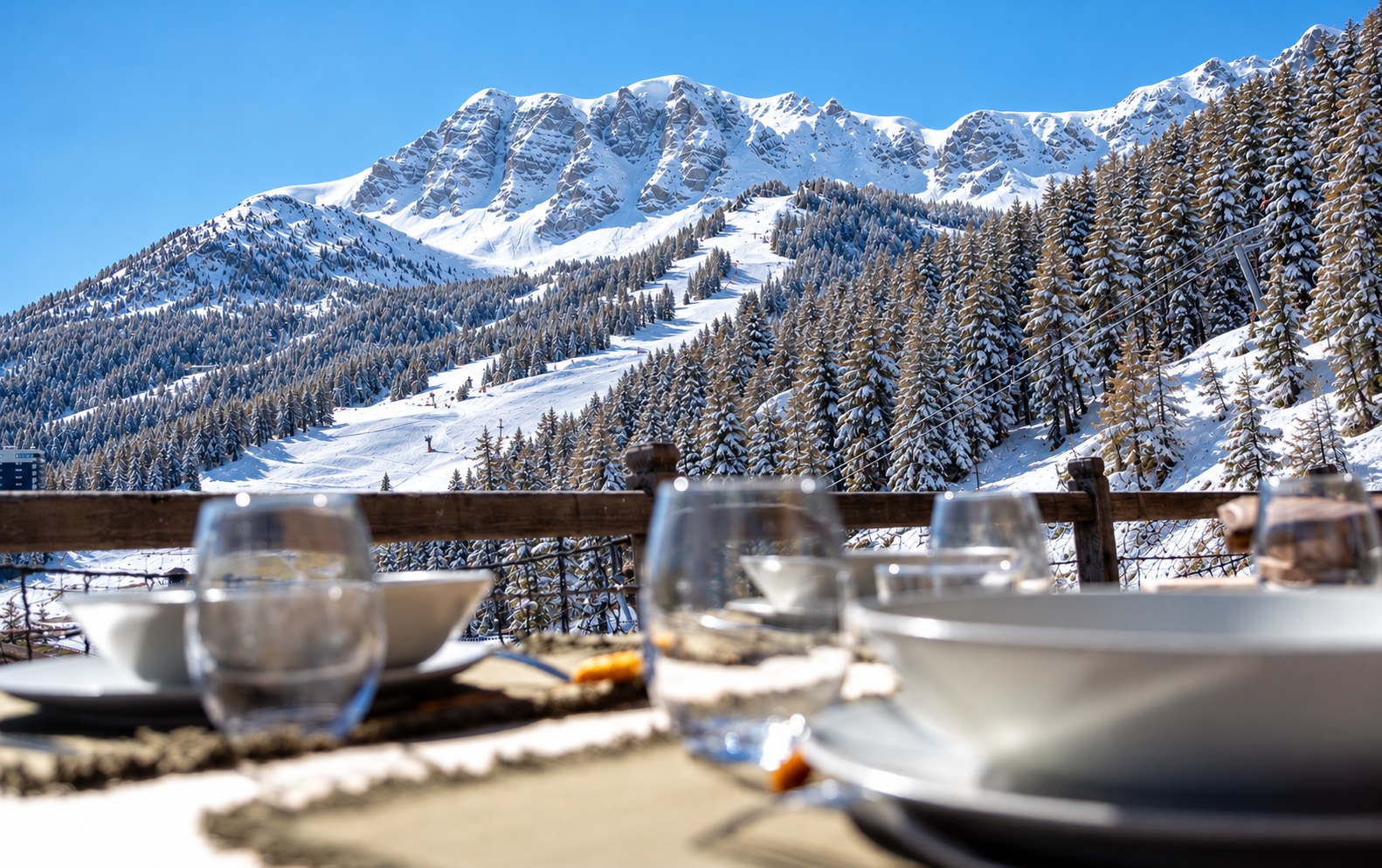 Table dressée sur une terrasse face aux montagnes et aux pistes enneigées
