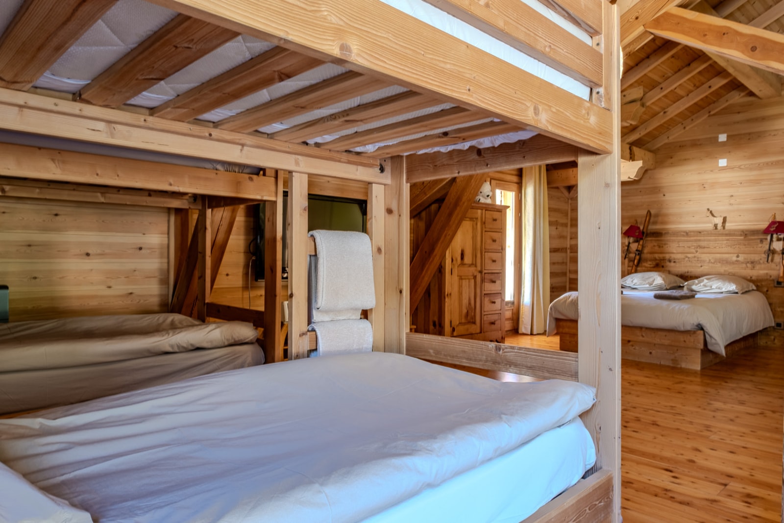 Dortoir en bois avec lits superposés, serviettes pliées et grand lit sous la charpente